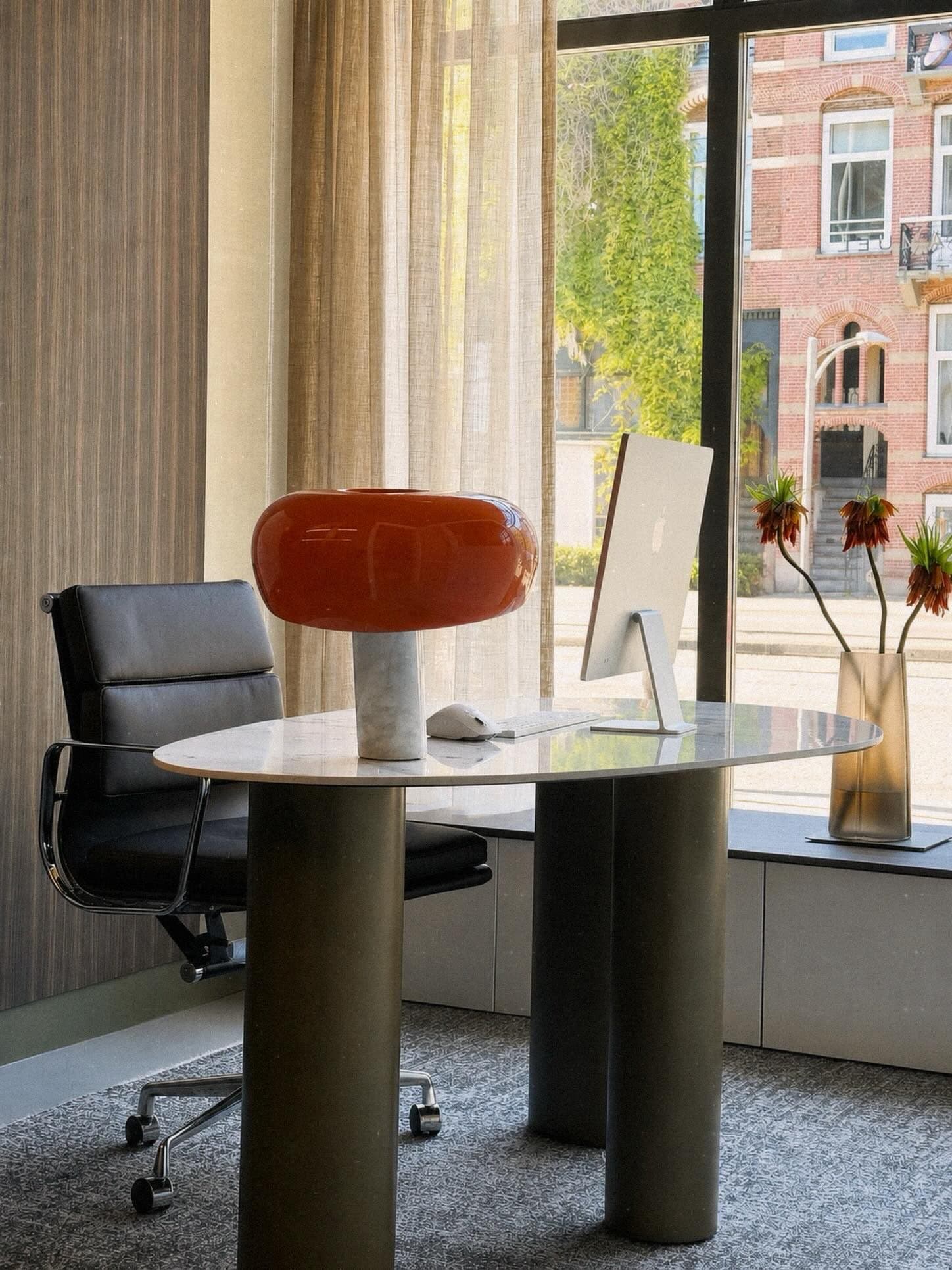 Werktafel in de studio met marmeren blad, bureaustoel en een computerscherm voor het raam
