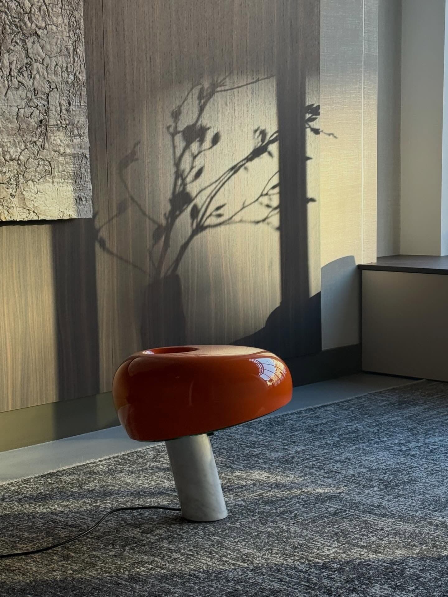 Detail in de studio: een oranje glazen tafellamp op een marmeren voet tegen een houten wand